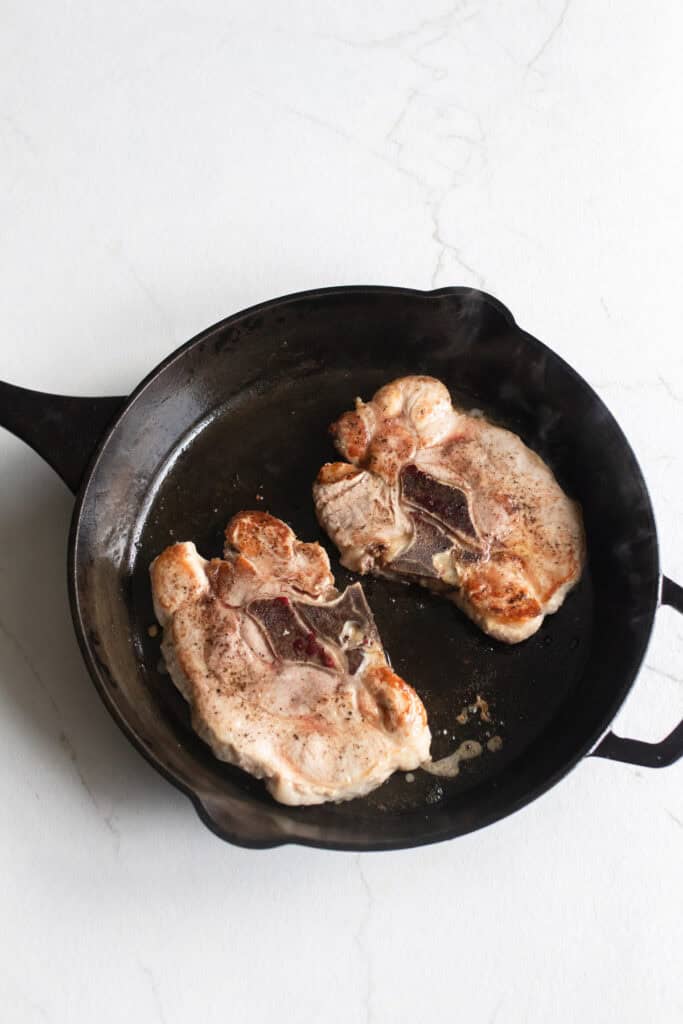 Cooking pork steaks in a cast iron skillet.