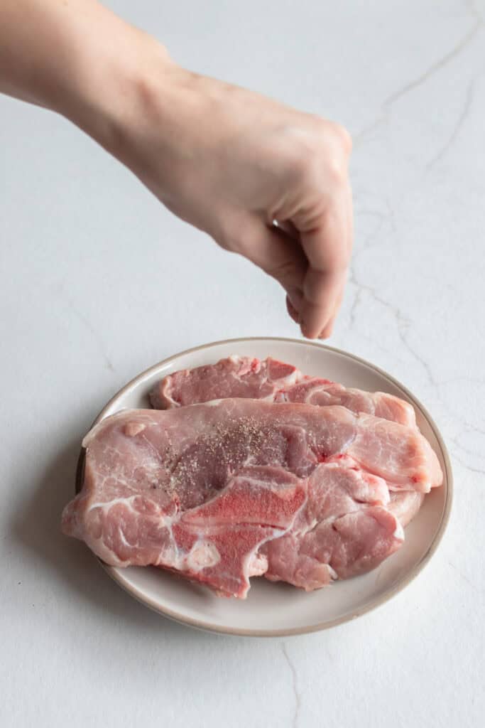 Sprinkling pork steaks with salt and pepper.