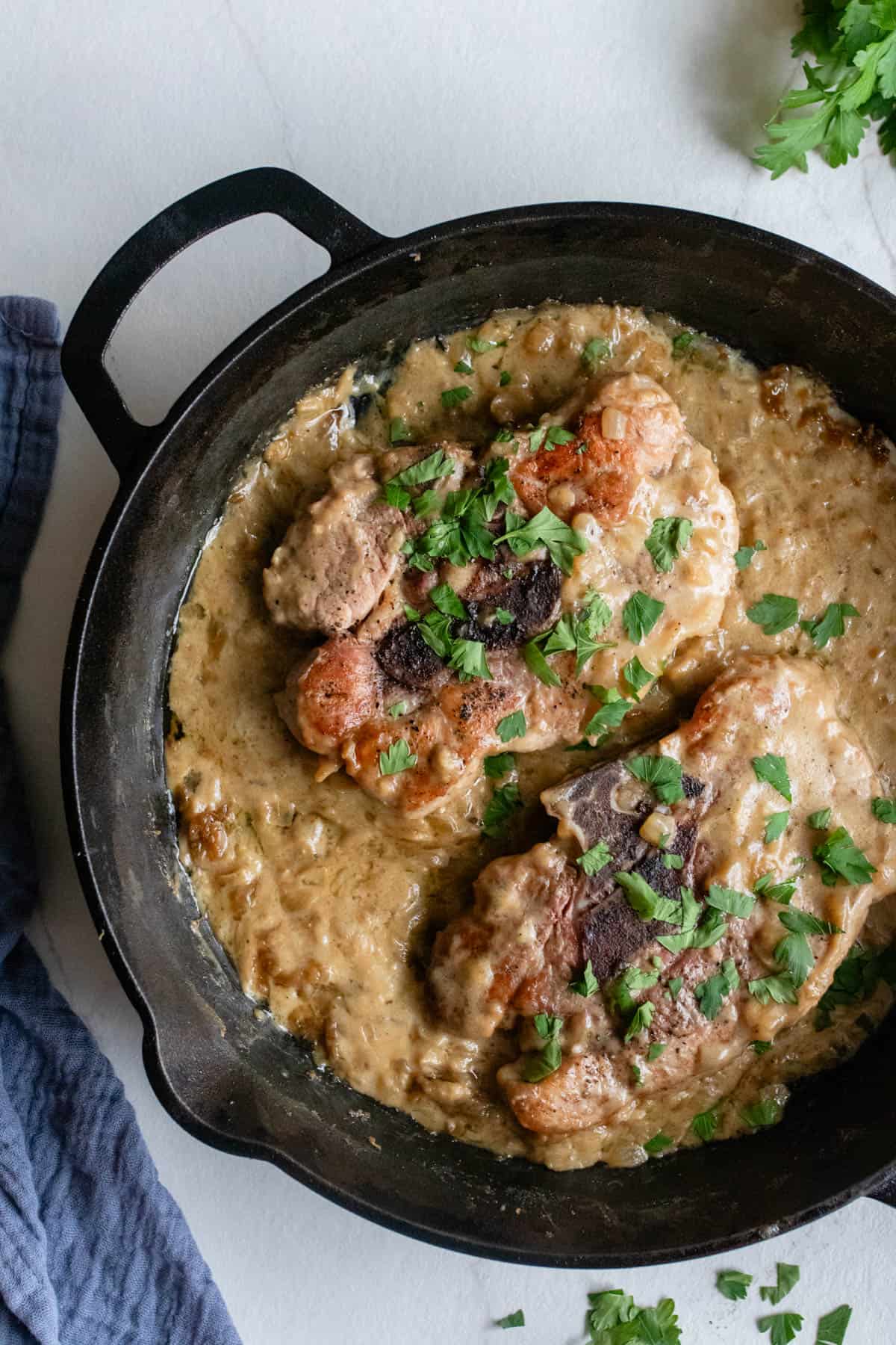 Pork steaks topped with fresh parsley in a creamy onion and garlic sauce in a cast iron skillet. 