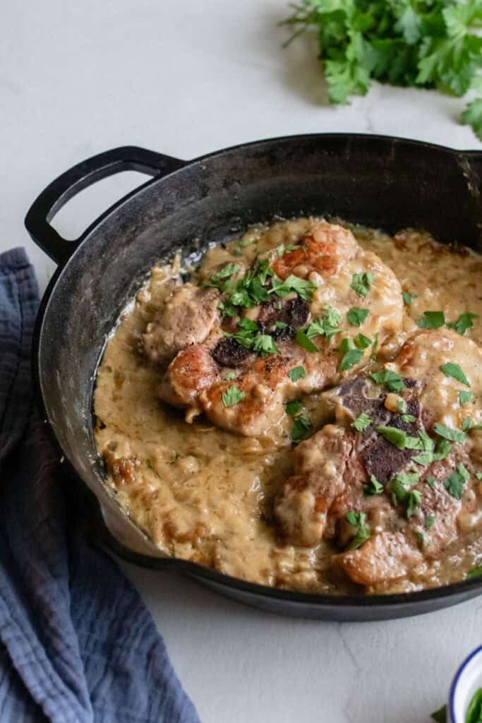 Pork steaks with creamy sauce in a cast iron skillet.