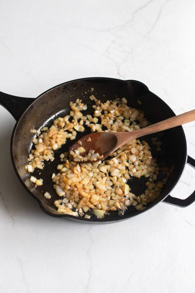 Sautéing butter, onions, and garlic in a cast iron skillet.