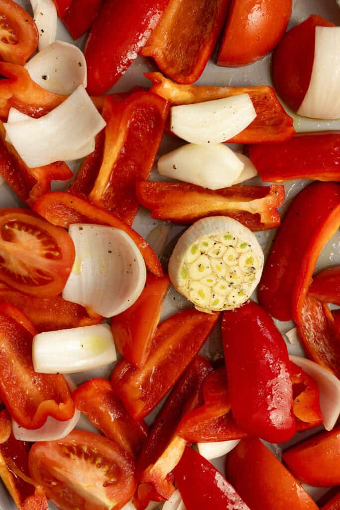 Roughly chopped tomatoes, onions, and red bell peppers on a baking sheet.