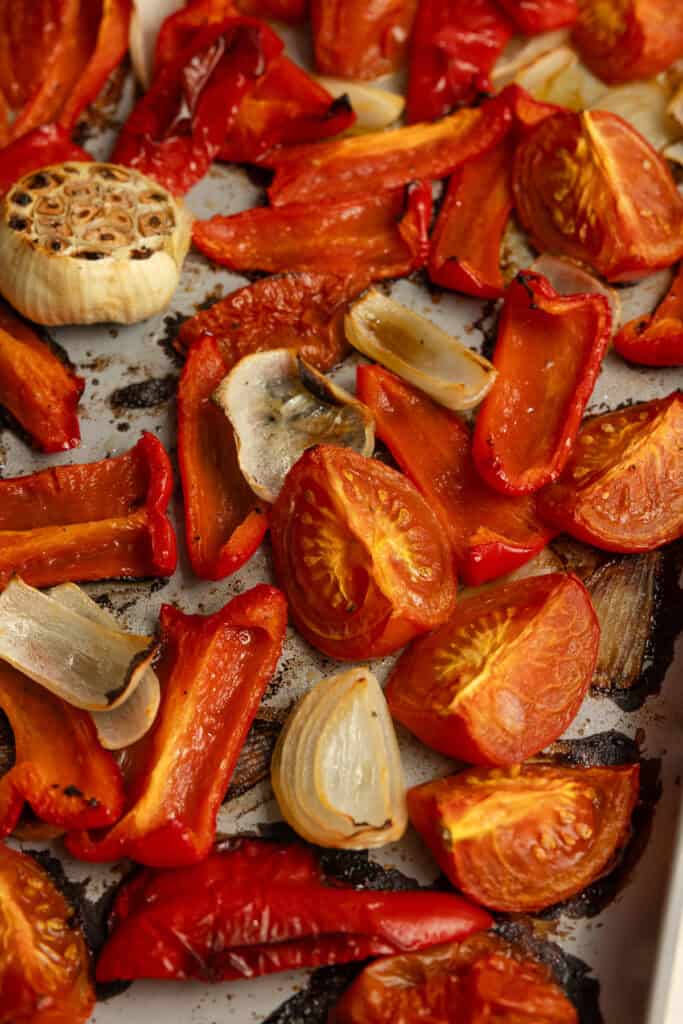 Tomatoes, peppers, garlic, and onion roasted on a baking sheet.