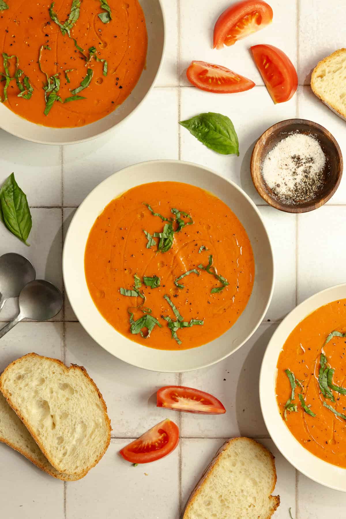 Three bowls of roasted red pepper and tomato soup topped with fresh basil. 