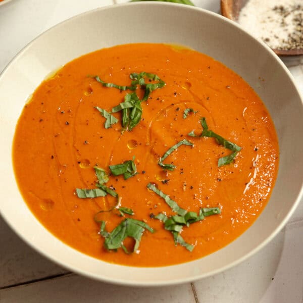 A bowl of roasted red pepper soup topped with fresh basil.