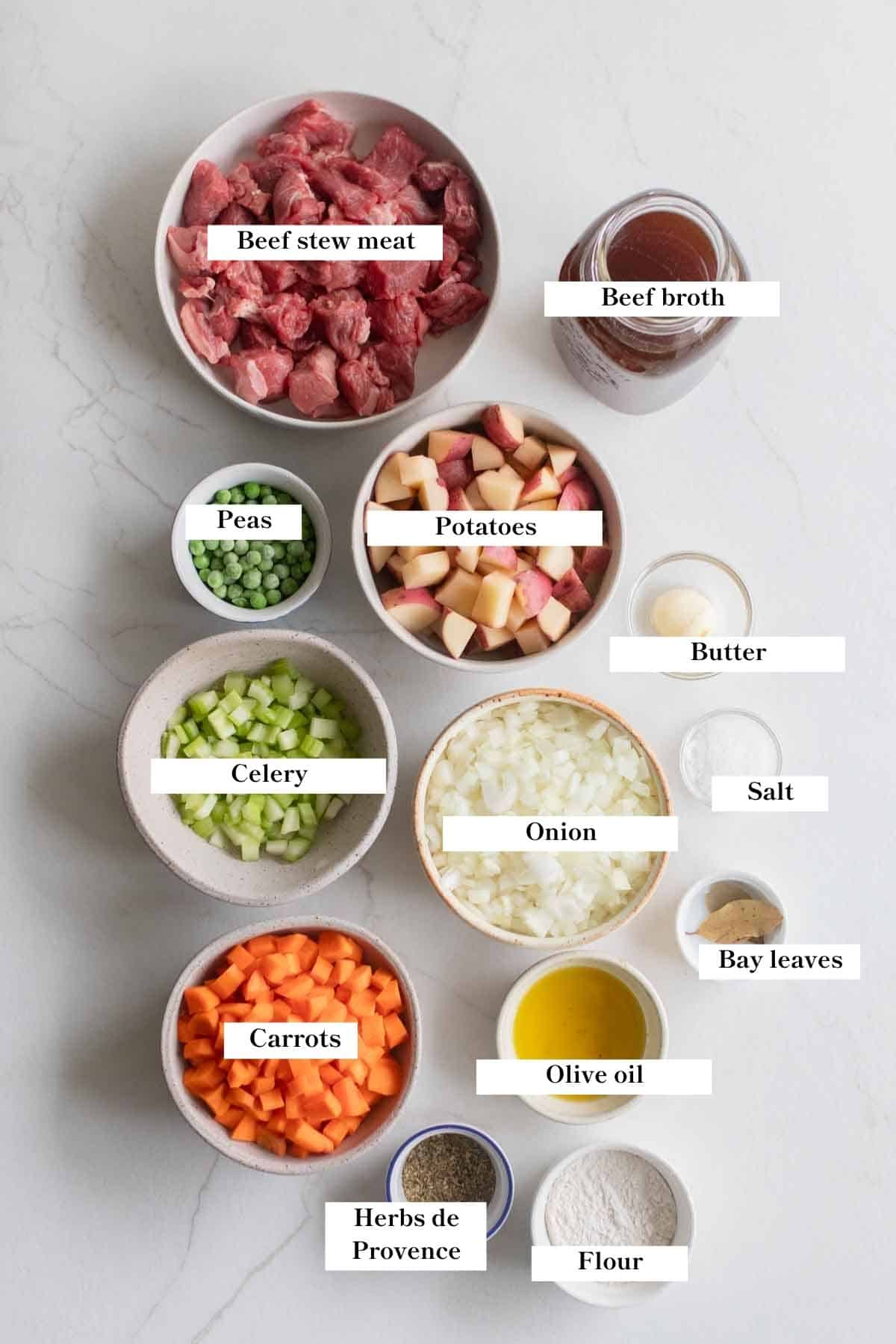 Ingredients for beef stew in bowls on a countertop. 