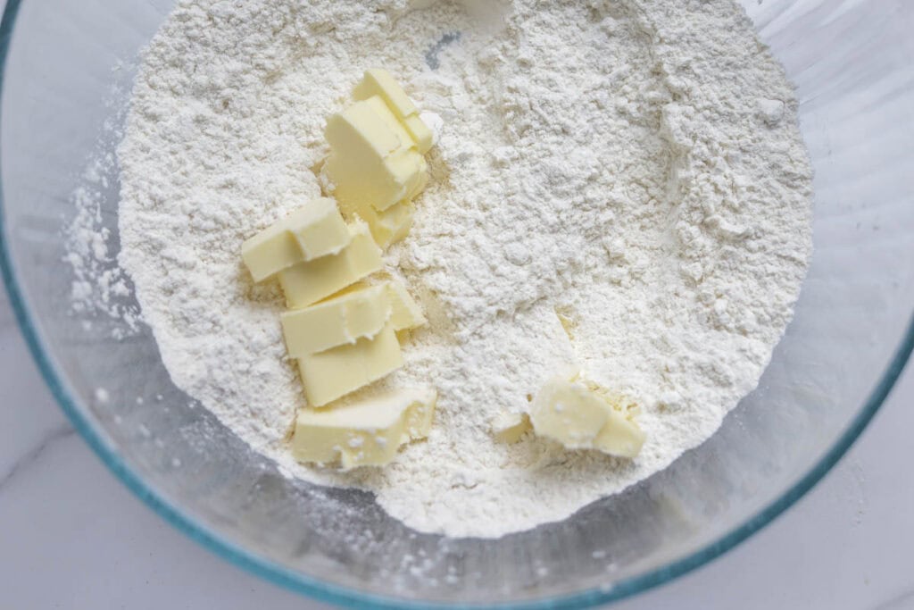 Chunks of butter added to dry ingredients in a bowl.