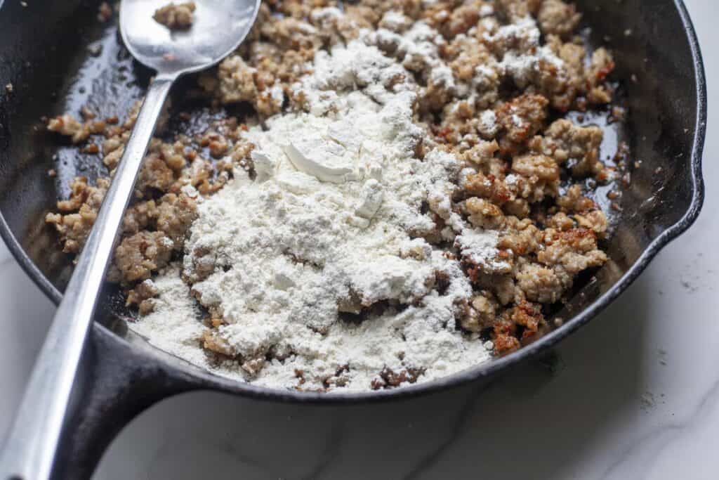 Flour sprinkled on brown meat in a cast iron pan.