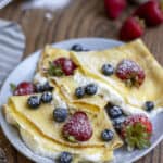 three sourdough crepes filled with whipped cream and berries on a gray plate.