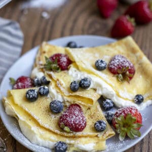 three sourdough crepes filled with whipped cream and berries on a gray plate.