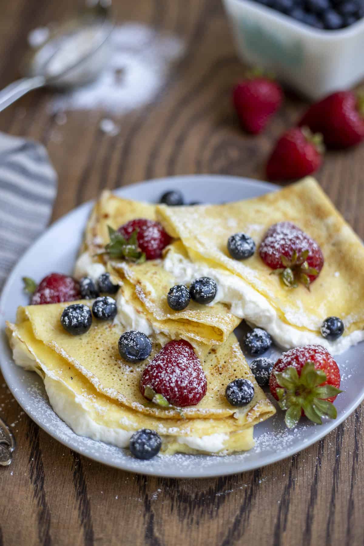 three sourdough crepes filled with whipped cream and berries on a gray plate.