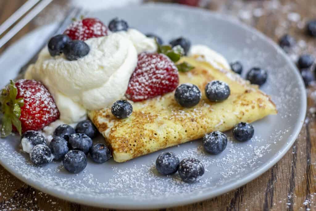 a gray plate with crepes with swirls of whipped cream cheese filling and fresh berries.