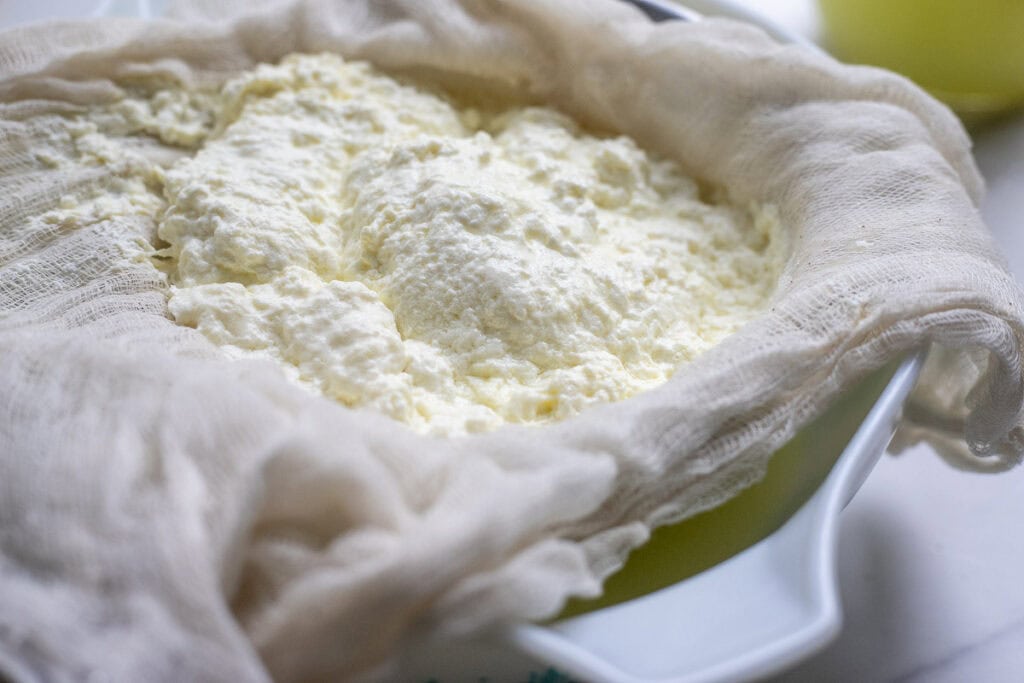 Curds straining in cheesecloth over a bowl.