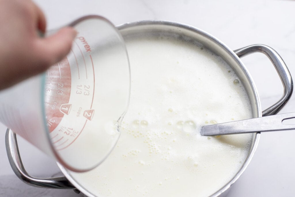 Adding white vinegar to a pot of milk.