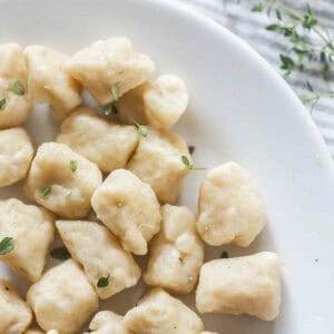 homemade gnocchi on a white plate topped with fresh parsley.