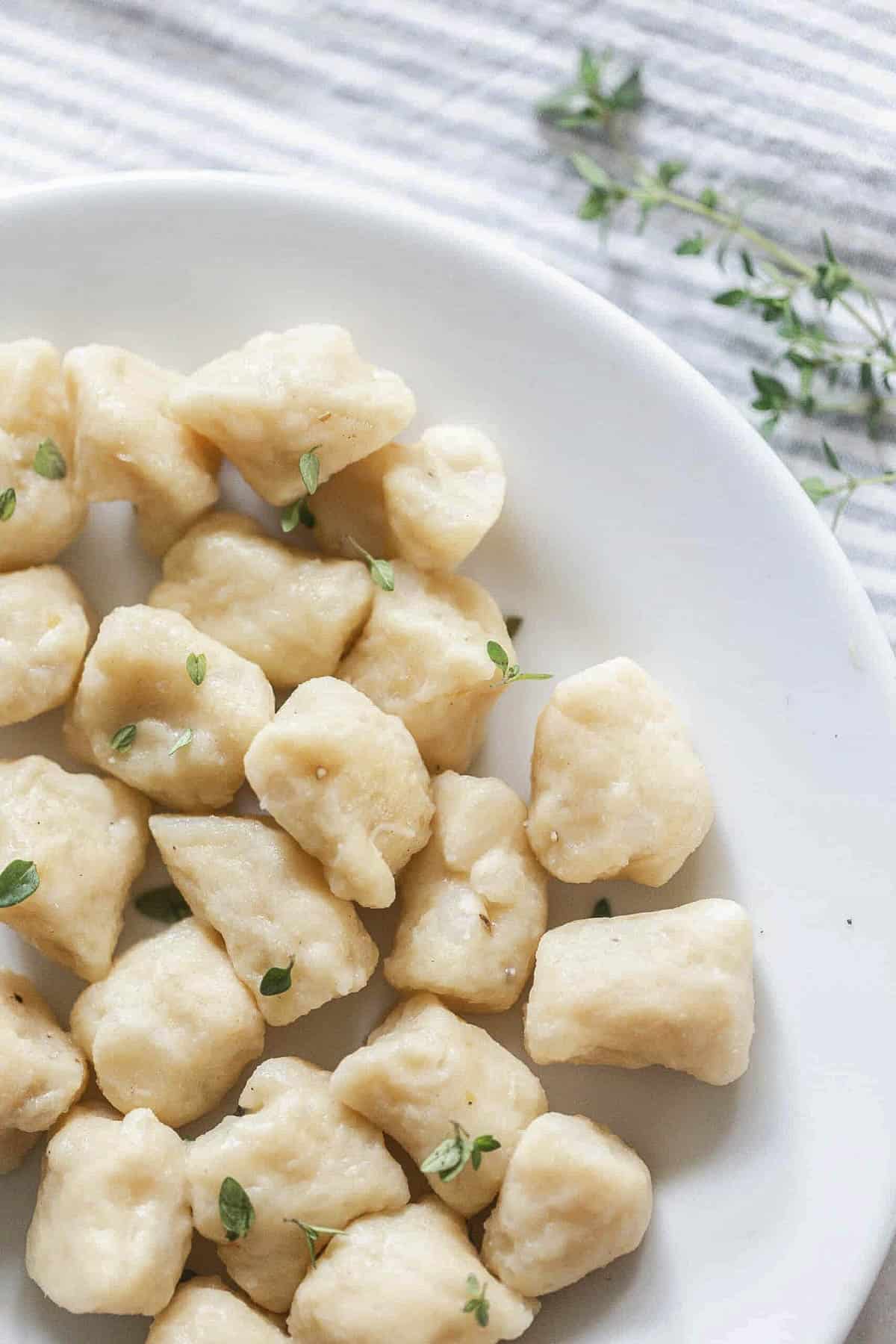 homemade gnocchi on a white plate topped with fresh parsley.