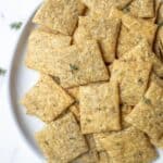 Overhead photo of sourdough crackers on a plate and topped with fresh herbs.