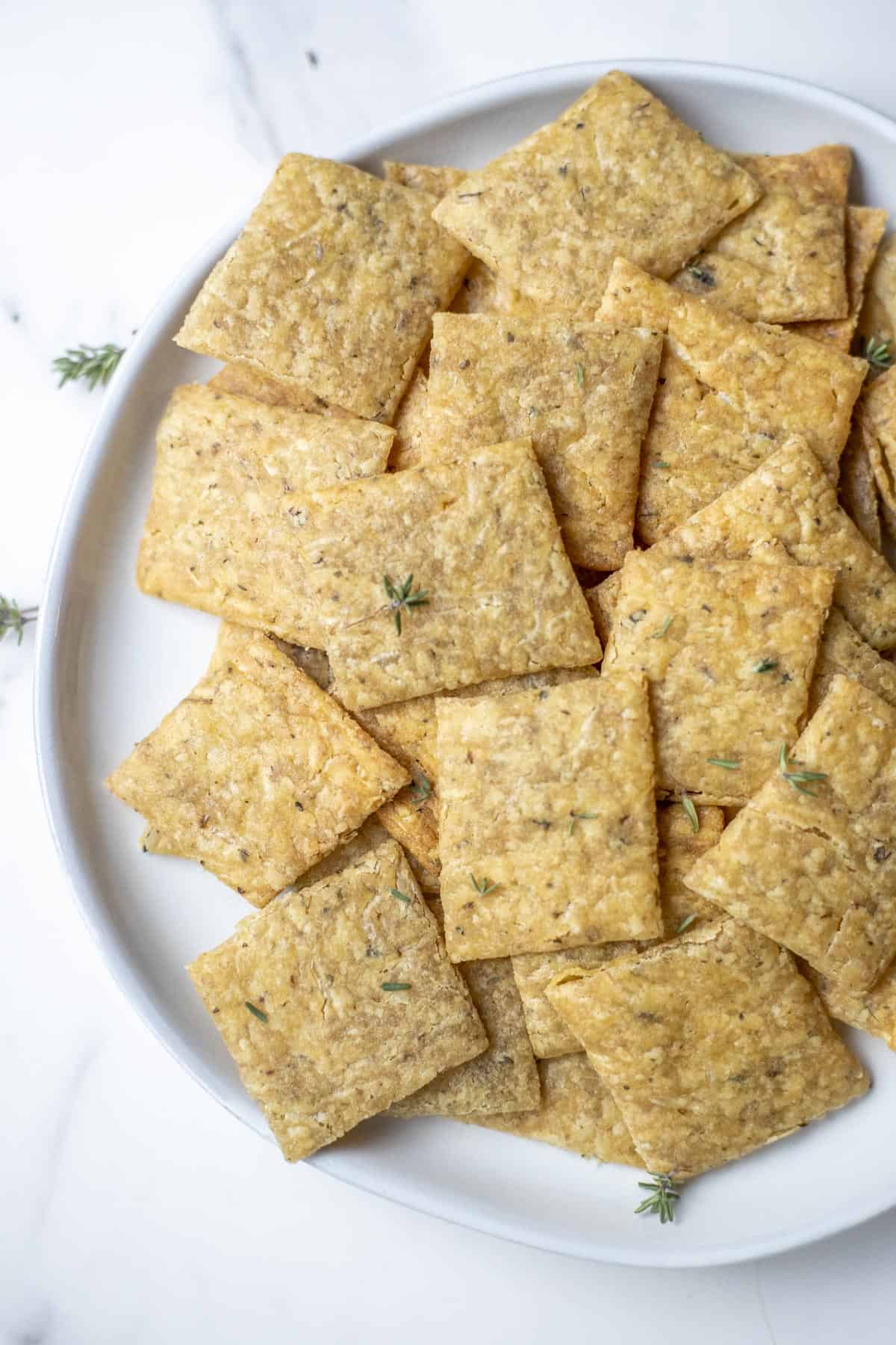 Overhead photo of sourdough crackers on a plate and topped with fresh herbs.