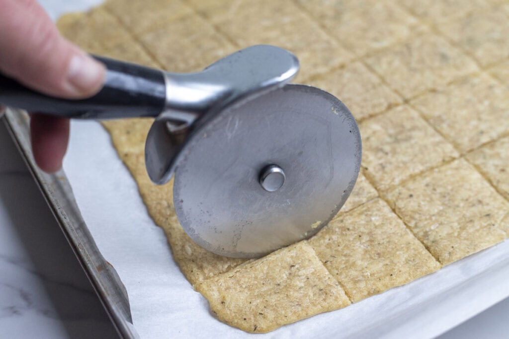 Cutting partially baked sourdough crackers with a pizza cutter.