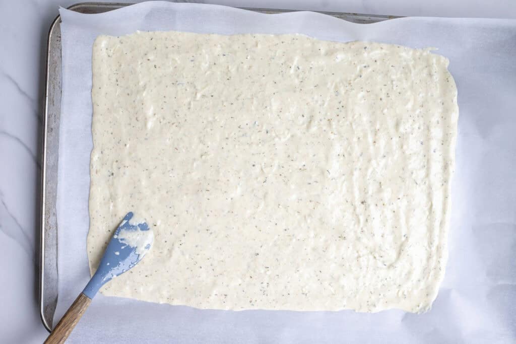 Cracker batter poured out on a parchment lined baking sheet.