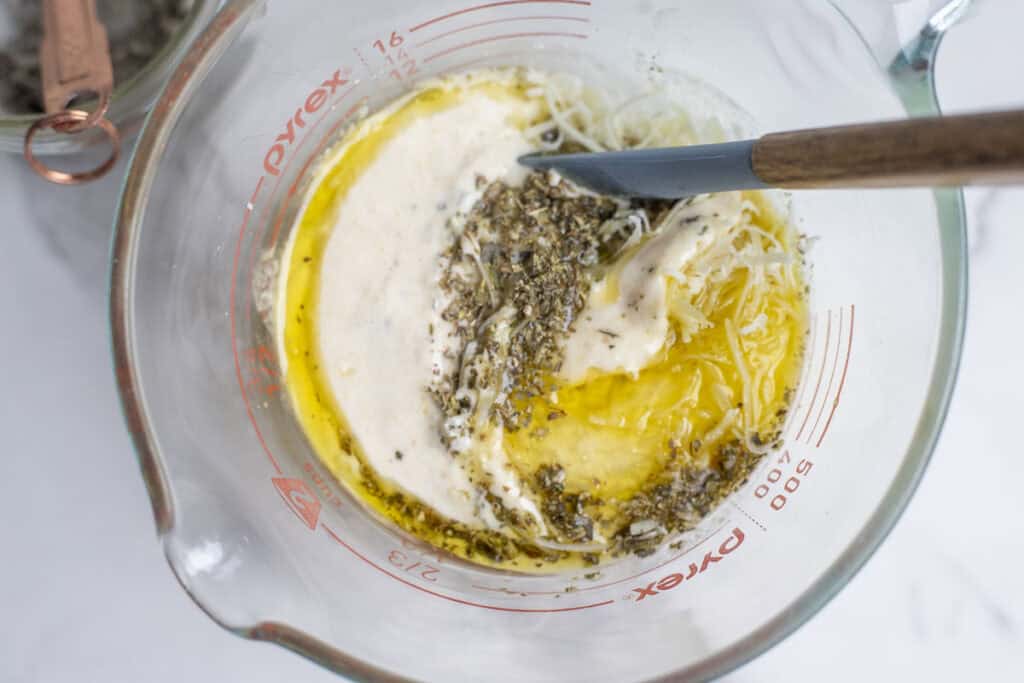 Adding sourdough starter, oil, and seasonings to a measuring cup.