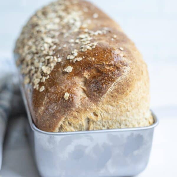 a loaf of sourdough oatmeal bread in a loaf pan on a countertop.