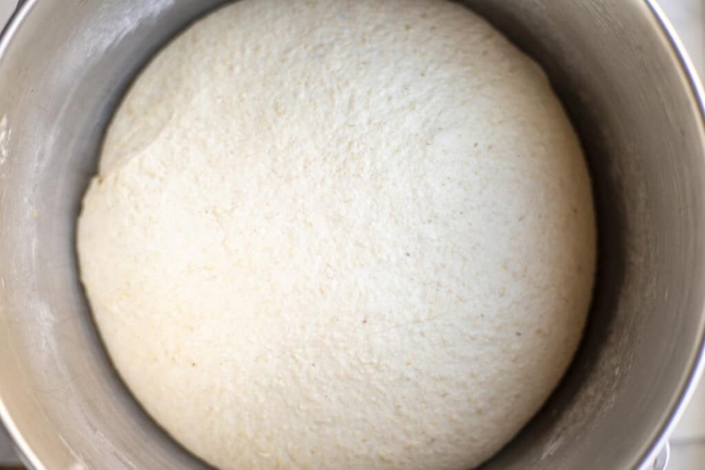 bread dough doubled in size in a metal bowl.