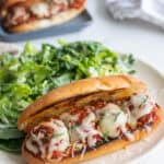 A plate with a meatball sub and salad.