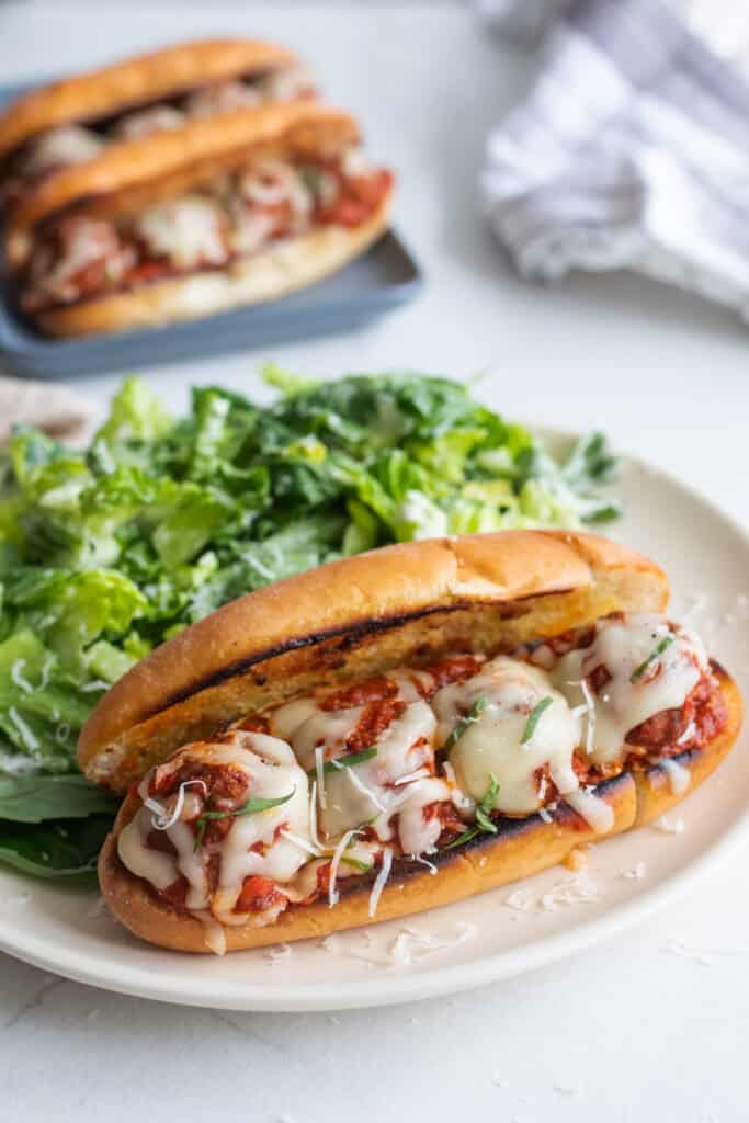 A plate with a meatball sub and salad. 