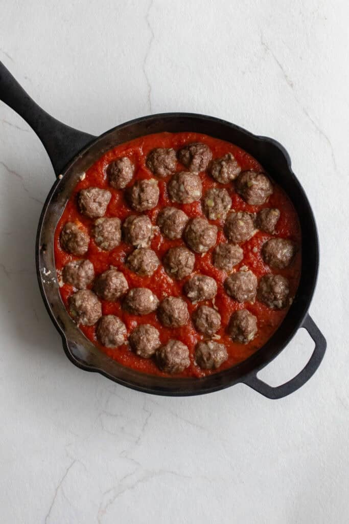 Meatballs in a marinara sauce in a cast iron skillet.