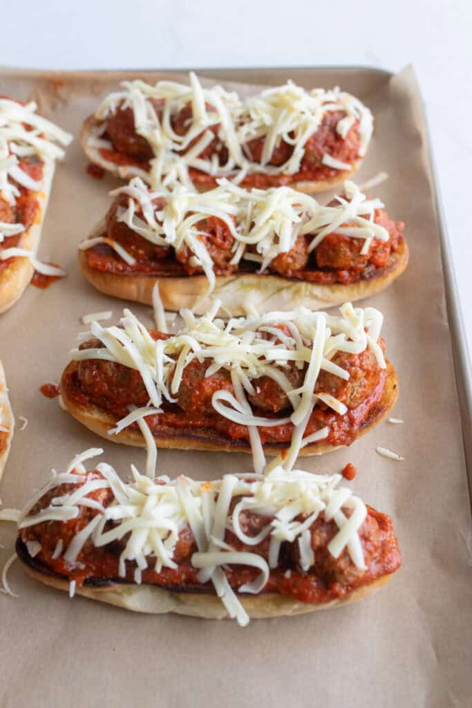 Four meatball subs on a baking sheet.