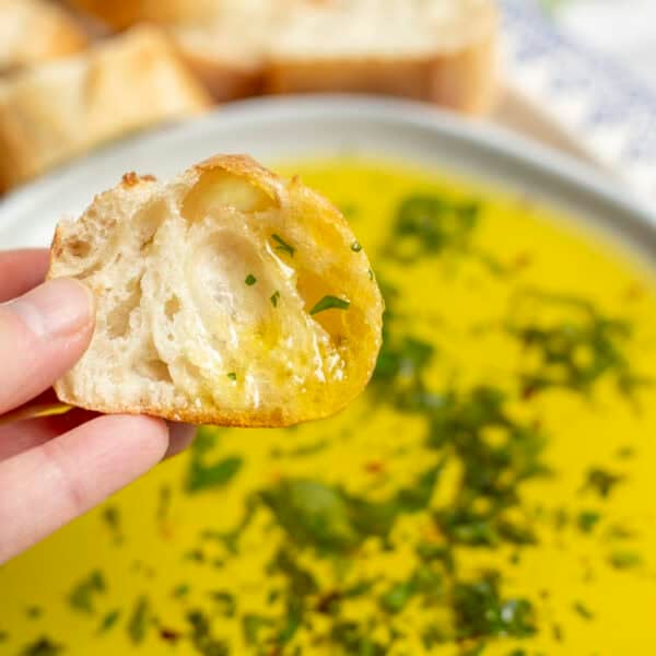 A hand holding a piece of bread dipping in oil.