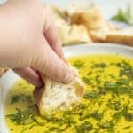 A hand dipping bread into oil and herbs.