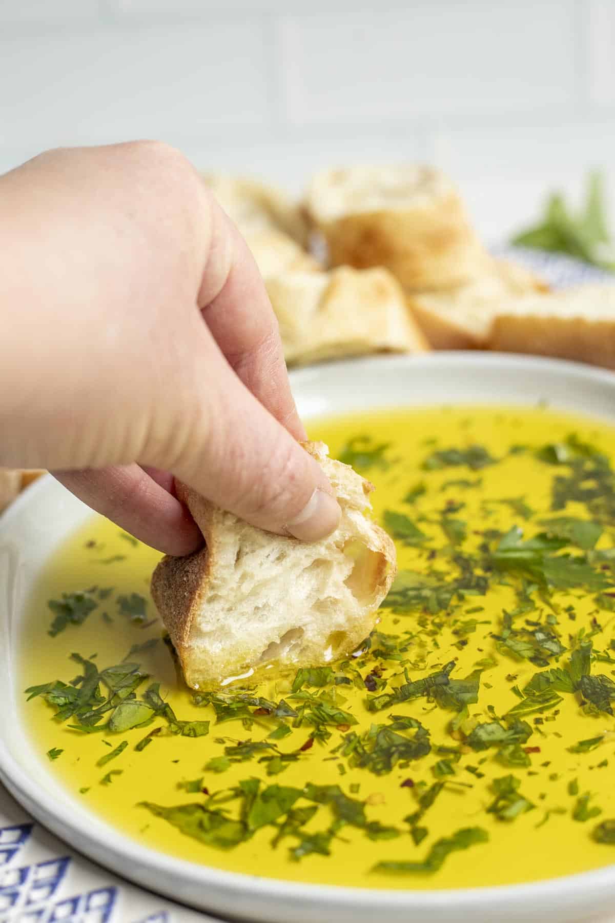 A hand dipping bread into oil and herbs.