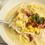 A bowl of chicken corn chowder with a spoon in it.