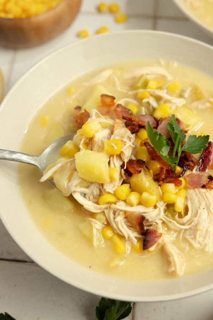 A bowl of chicken corn chowder with a spoon in it. 