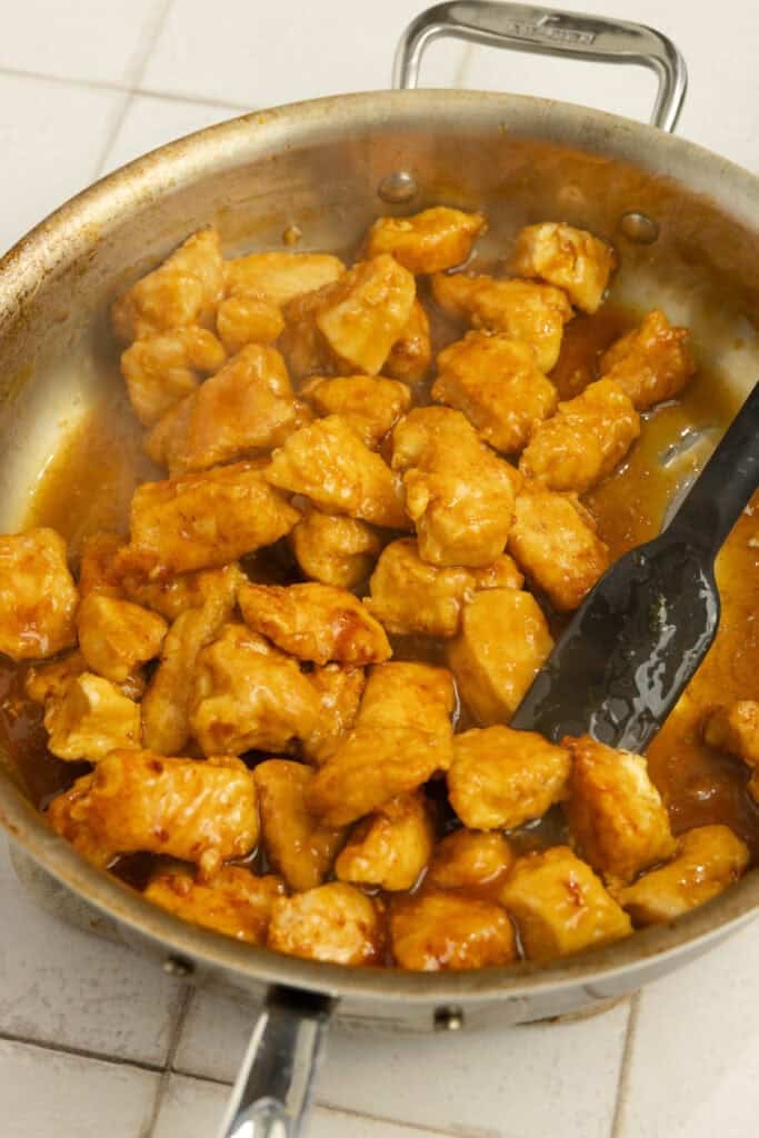 Cubed chicken tossed in an orange sauce in a saucepan.