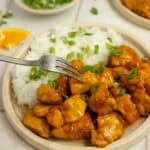 A fork on a plate with orange chicken and rice.