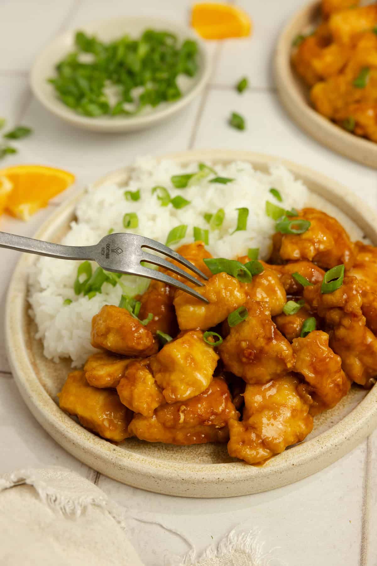 A fork on a plate with orange chicken and rice.