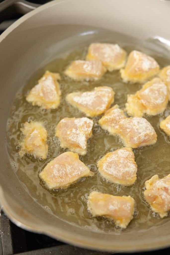 Chunks of coated chicken in a pan of oil.