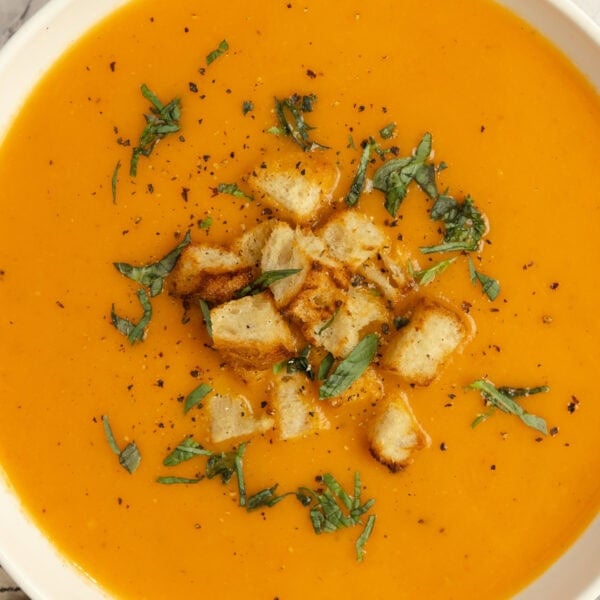 A bowl of tomato soup with croutons and herbs sprinkled on top.