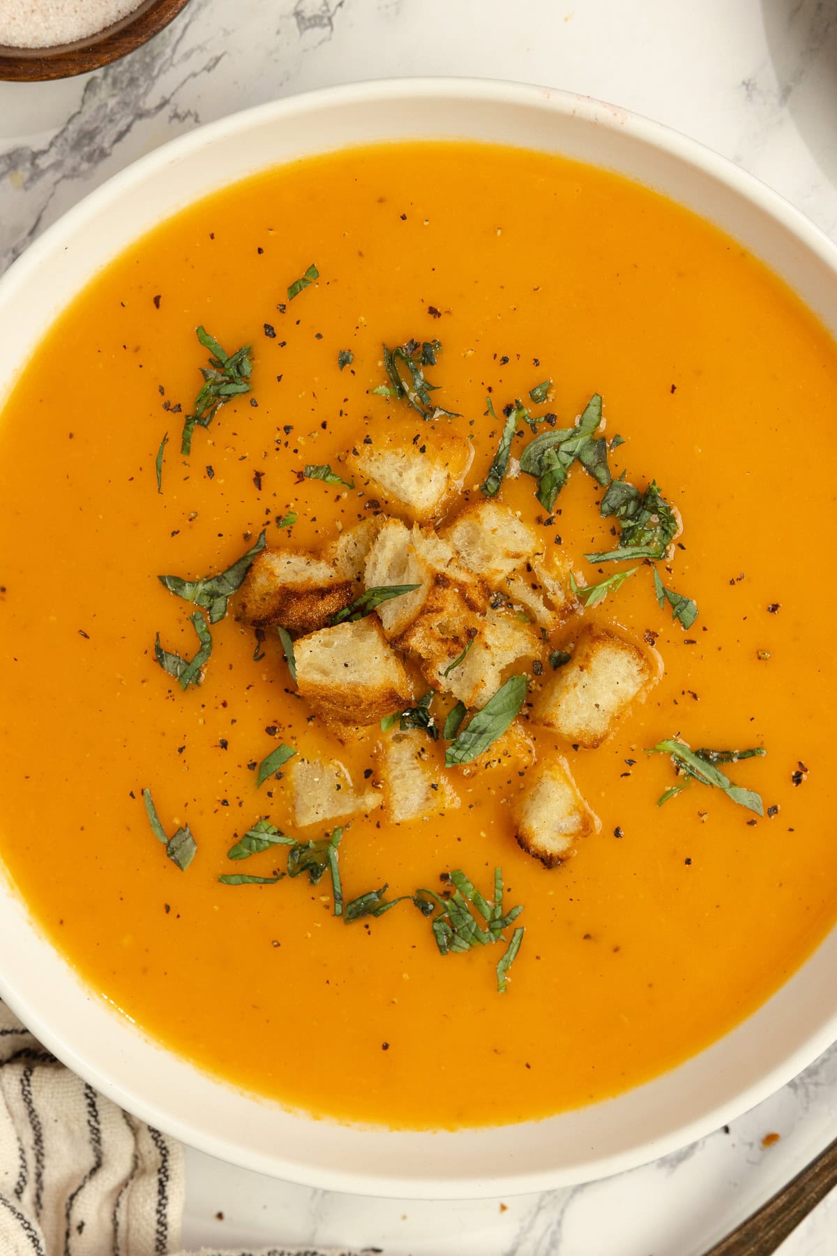 A bowl of tomato soup with croutons and herbs sprinkled on top.