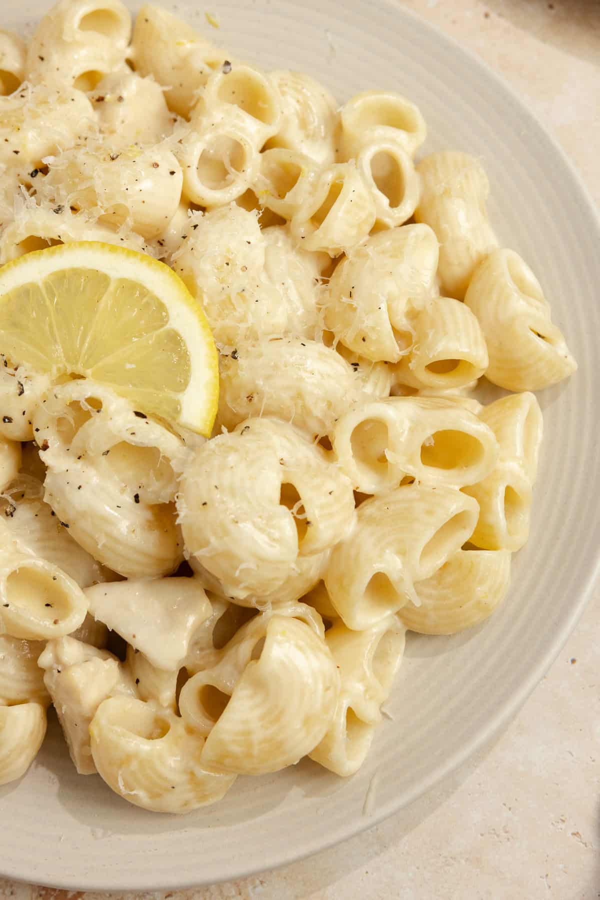 Pasta with a cream sauce, chicken and lemon wedge on a plate.