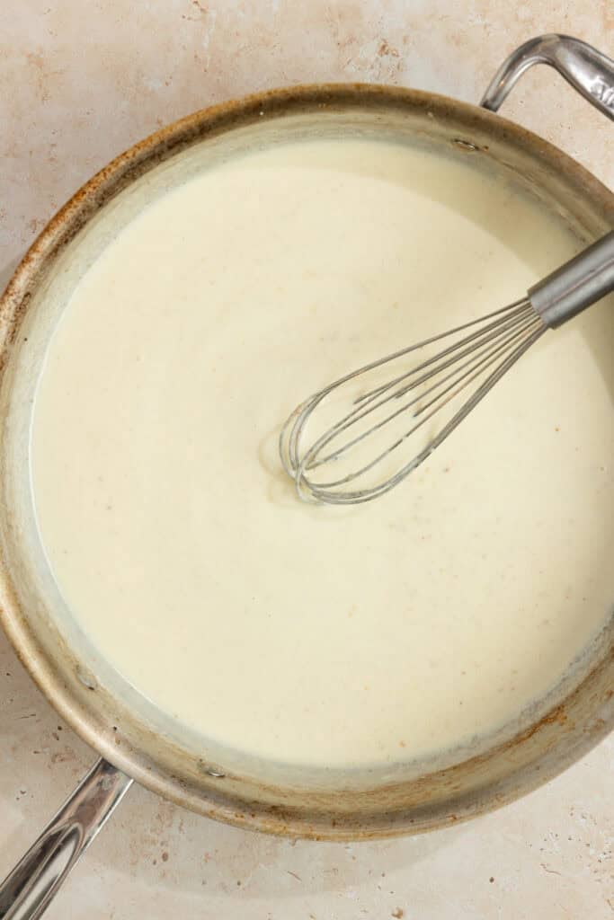 Cream added to a skillet with a whisk. 