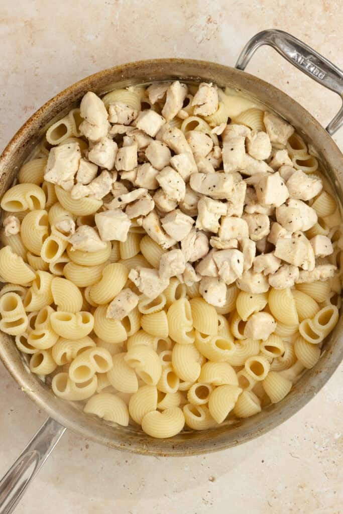 Cooked chicken and pasta added to sauce in a skillet. 