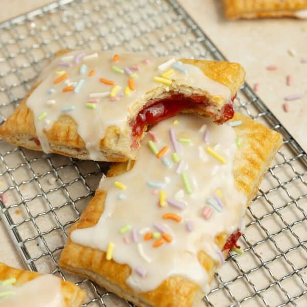 two homemade pop tarts topped with icing and sprinkles on a wire rack.