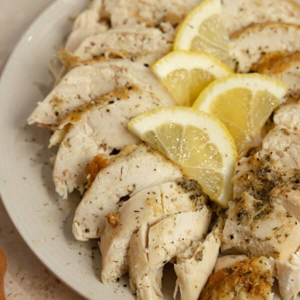 Whole chicken cut up on a plate with lemon wedges on top.